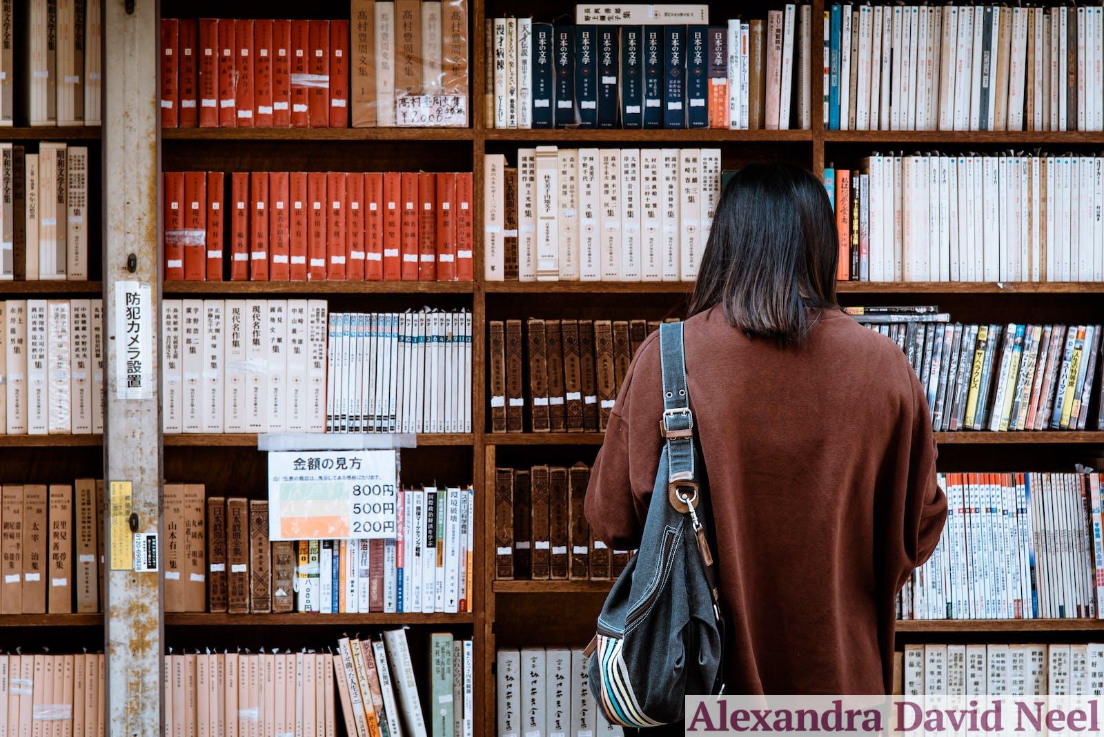 Woman Wearing Brown Shirt Carrying Black Leather Bag on Front of Library Books